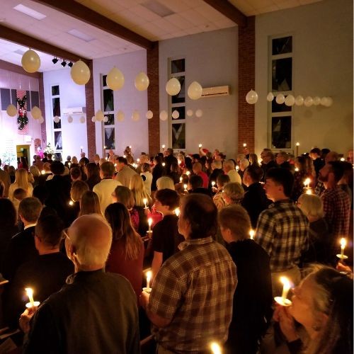 A large group of Christians holding lit candles in a dark church on Christmas Eve