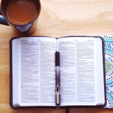 An open bible on a desk with a mug of coffee at the top left corner